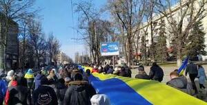 　３月、ウクライナ南部ヘルソンで、国旗と同じ色の横断幕を運ぶデモ隊（ロイター＝共同）