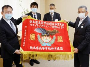 贈られた女子重量挙げの優勝旗を披露する県高体連の金本会長(左)ら=徳島新聞社