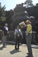 にっぽん丸の乗客に巨大タヌキ像を紹介するボランティアガイド（右）＝小松島市小松島町の小松島ステーションパーク