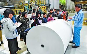 新聞用紙の前で、大きさなどの説明を受ける参加者=愛媛県四国中央市の大王製紙三島工場