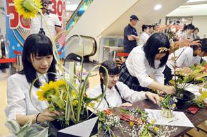 ヒマワリなど夏らしい花材を使って作品を仕上げる生徒たち＝徳島市のアミコ専門店街