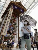 　夏を彩る「飾り山笠」（左）の前を日傘を差して歩く女性＝２日午後、福岡市