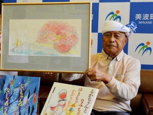 寄贈した絵本の原画を持つ山内さん。手前は絵本「ひわさの四季シリーズ」=美波町役場