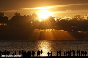 雲の切れ間から現れた初日の出に歓声を上げる見物客＝１日午前７時26分、徳島市の小松海岸