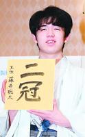 「二冠」と書かれた色紙を手に、笑顔を見せる藤井聡太新王位=20日、福岡市内のホテル