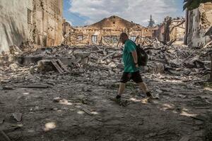 　ウクライナ東部ルガンスク州リシチャンスクで、攻撃を受け破壊された建物の前を歩く人＝６月（ロイター＝共同）