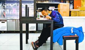 北京市内のフードコートで昼食を取る市民。新型コロナウイルス対策で、テーブルに客が向かい合わせで座らないように片側の椅子が机の上に置かれていた=3月25日(共同)